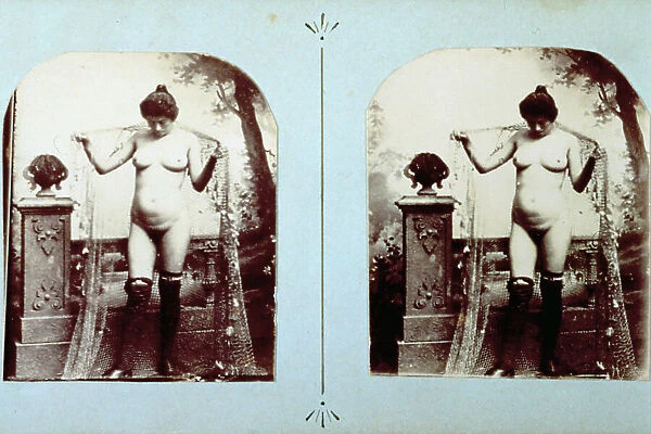 Studio photograph of a full-length female nude. She is wearing long stockings. Behind her afFishing net