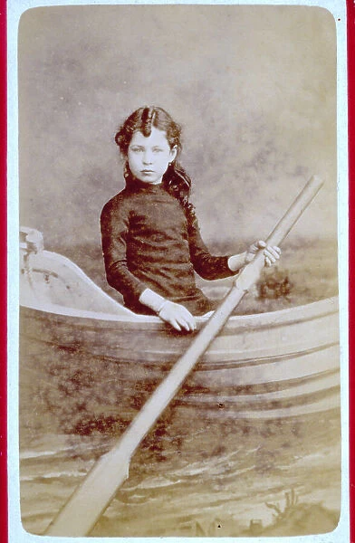 Studio portrait of a little girl behind a screen on which a boat is painted. She holds an oar