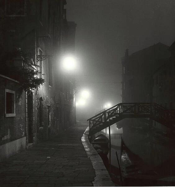 View of a desert Venetian fondamenta wrapped in a foggy night. On the right a small, private, wooden bridge built on the Rio Ognissanti