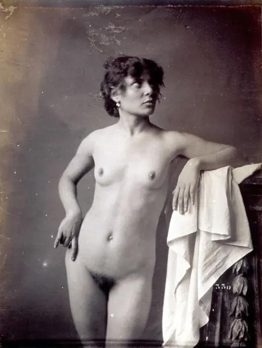 Framed Print : Young model shown, nude, in the studio. She is posing with her left arm resting on a pedestal covered by a light cloth and with her head facing to one side Framed Print : Young model shown, nude, in the studio. She is posing with her left arm resting on a pedestal covered by a light cloth and with her head facing to one side