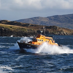 Valentia severn class lifeboat John and Margaret Doig 17-07. Lifeboat is moving from right to left in choppy seas, lots of white spray and waves breaking against cliffs in the background
