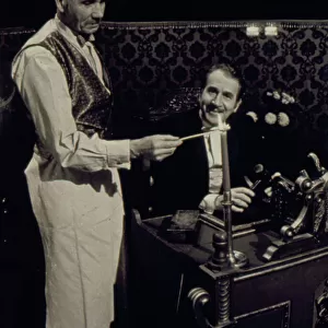 Two of the cast of the Old Time Music Hall TV show, known as The Good Old Days, filmed at the City Varieties in Leeds. The man on the left lights a candle, while the compere, played by the actor Leonard Sachs, smiles benignly. Date: 1960s