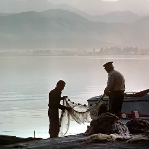Two fishermen sort their nets on stone quayside - Fetheye