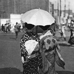 Two Japanese women walk holding a parasol