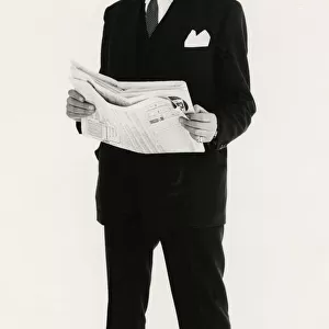 Full length portrait of a mature man posing in a suit, holding a newspaper