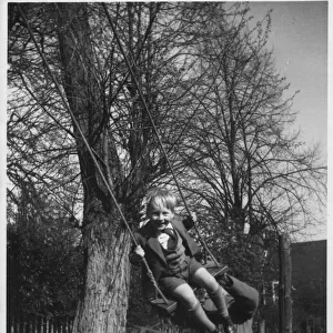 A little boy being pushed on a swing. Date: c. 1950