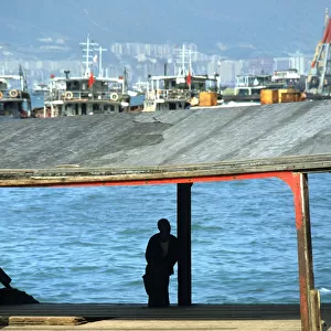 Silhouette of man sat on a bollard on a pier in Hong Kong