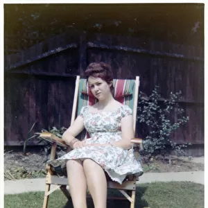 A young lady sat in a neat garden in a canvas-backed chair