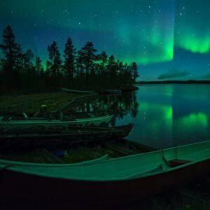 Beached canoes and Aurora Borealis and stars reflected in lake at night, Muonio, Lapland