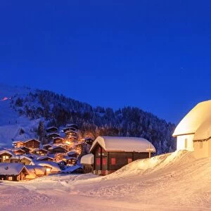 Blue dusk on the alpine village and church covered with snow, Bettmeralp, district of Raron