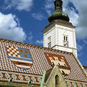 Close-up of tile roof with pattern of shields and clock tower of St. Marks church