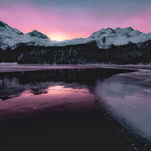 Colorful sky at sunrise on snowcapped mountains and frozen Lake Silvaplana, Maloja
