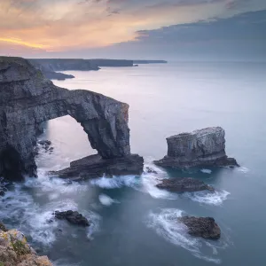 Colourful dawn sky above the Green Bridge of Wales natural arch in Pembrokeshire, Wales