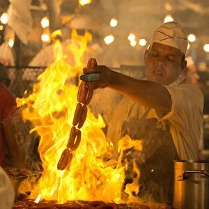 Local man cooking sausages on open flame at one of the food stalls in the Djemaa el Fna