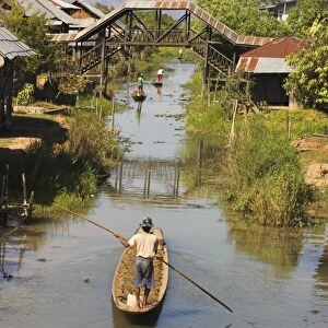 Men standing up paddling canoes through floating village, Inle Lake, Shan State