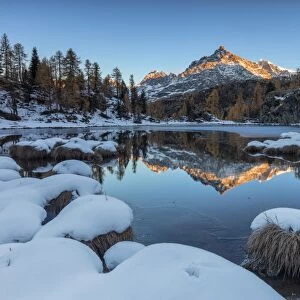 The rocky peak reflected in the frozen Lake Mufule at dawn, Malenco Valley, Province of Sondrio