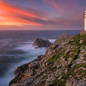 Sea landscape view of Cape Tourinan Lighthouse at sunset with pink clouds, Galicia, Spain