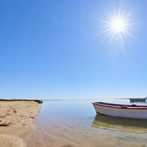 The sun shines above a small fishing boat on transparent lagoon water in Cacela Velha
