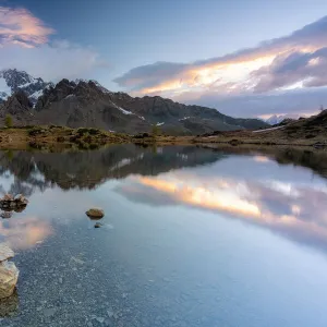 Sunrise lit the rocky peak of Monte Disgrazia mirrored in the clear water of lake Zana