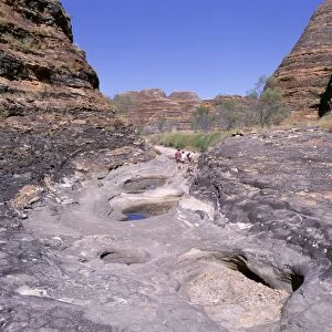 Tourists cross flood scoured rocks, past typical formations, Purnululu National Park