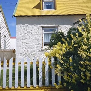 Typical house, with yellow corrugated roof and white stone walls and fence