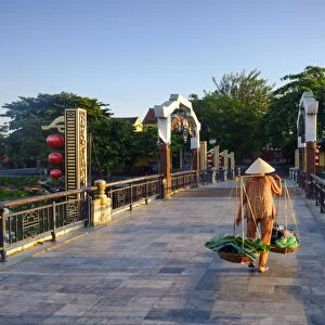 A woman carrying baskets on a yoke over the Lantern Bridge in Hoi An, Quang Nam, Vietnam