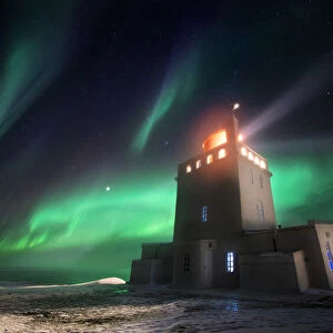 Dyrholaey lighthouse in winter with aurora borealis dancing above it, Sudurland, Iceland