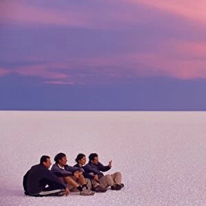 A group of tourists sit on the great expanse of salt
