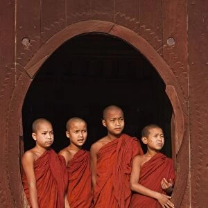 Myanmar, Burma, Nyaungshwe. Young novice monks standing at a wooden oval window