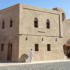 An Omani man walks in front of a restored building in Bahla Fort, Tanuf, Oman
