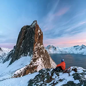 One person contemplating the sky at sunset sitting on a snowy ridge on Segla mountain, Senja, Troms county, Norway