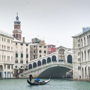 Rialto bridge, Venice, Veneto, Italy. Tourists on gondola under a snowfall