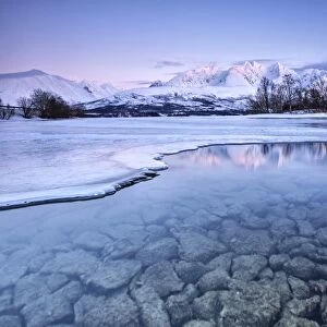 Snowy peaks are reflected in the frozen Lake Jaegervatnet at sunset Stortind Lyngen Alps Tromsa¸ Lapland Norway Europe