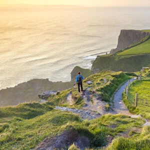 A tourist admiring the view of a sunset at the Cliffs of Moher