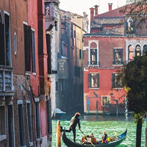 Venice, Veneto, Italy. Tourists on a gondola in a backstreet canal