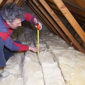 A man measuring the depth of insulation in a house loft or roof space. Insulating your loft can save a significant amount of household heat loss and therefore help save energy and help combat climate