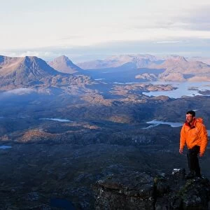A mountaineer on Suilven summit at Dawn in Scotland UK looking towards Stac Polaidh and Cul Mhor