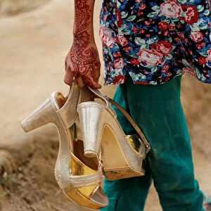 A Bangladeshi girl carries her older sisters golden shoes as their family visits