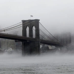The Brooklyn Bridge is seen partially in fog from in front of the Manhattan skyline