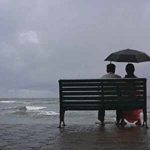 A couple rests on a seaside promenade during a rain shower in Kochi