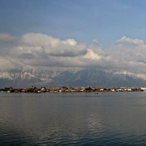 Kashmiri man rows boat on Dal Lake surrounded by snow-covered mountains in Srinagar