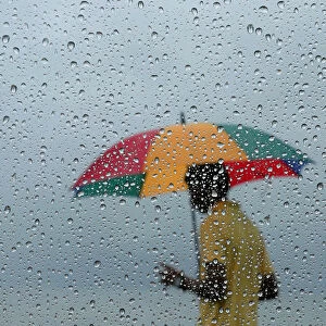 A man carrying an umbrella is seen through a window covered with rain drops during a wet