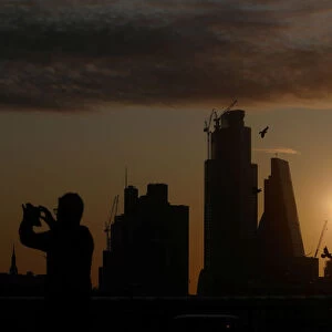 A man takes a photograph of the skyline as the sun rises behind the city of London