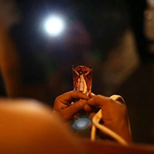 A masked penitent prays as he holds an image of Jesus Christ during a procession as part