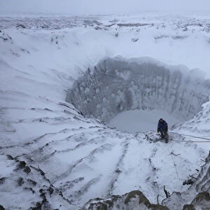 A member of an expedition group stands on the edge of a newly formed crater on the Yamal Peninsula