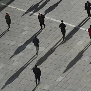 People cast long shadows in the winter sunlight as they walk across a plaza in the