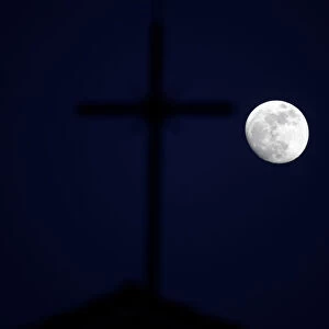 The super moon full moon is seen in front of the cross of a church in Siero