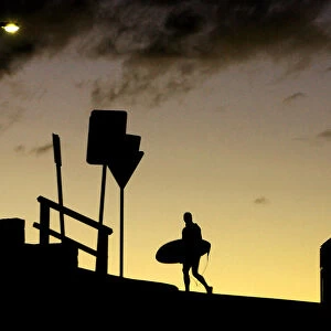 A surfer crosses the road with his board at sunset above Sydneys Bondi Beach