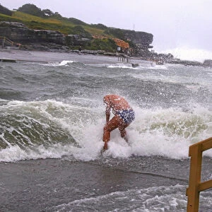A swimmer is hit by wave as he enters the water in severe weather in Sydney