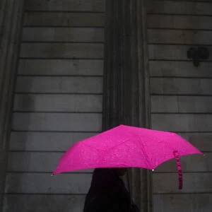A woman carries an umbrella during a rain shower as she walks past the Bank of England
